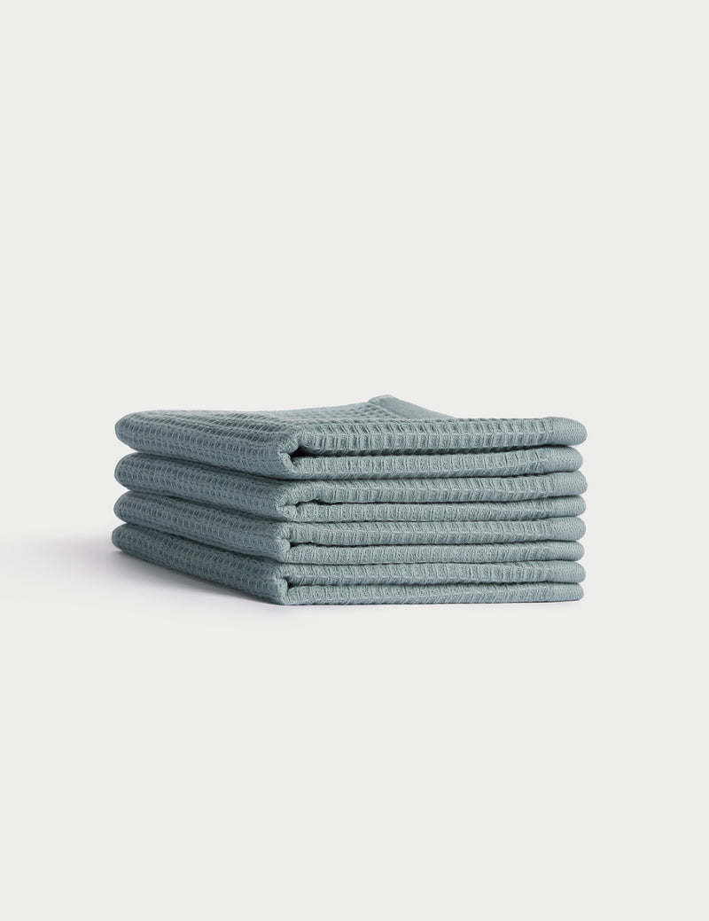 A stack of five neatly folded light blue Cozy Earth Waffle Washcloths is displayed against a plain white background.