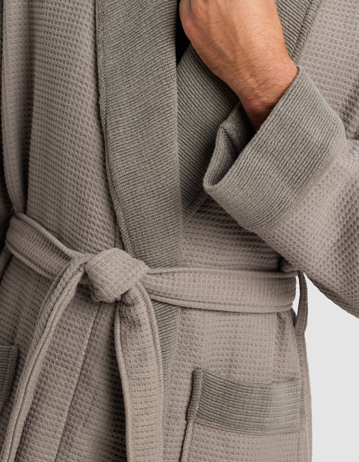A person wears the Cozy Earth Waffle Bath Robe in light gray, featuring a textured design, shawl collar, waist tie, and two front pockets, with one hand holding the collar.