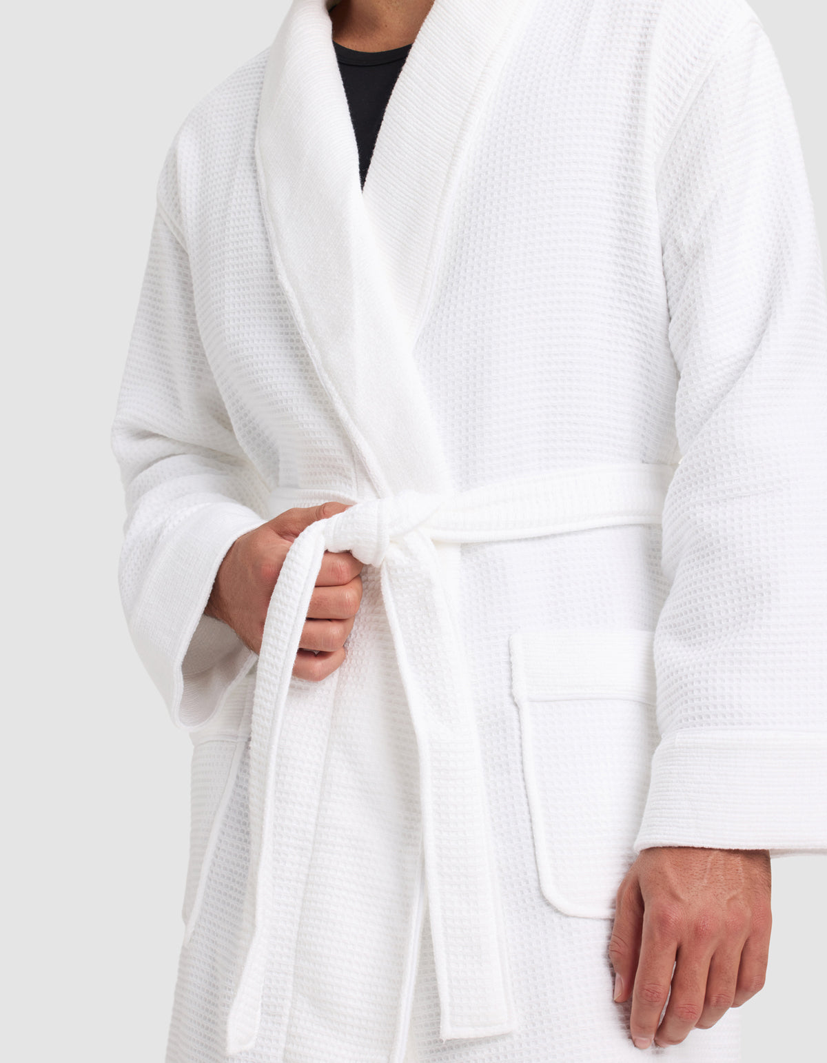 A person wears the Cozy Earth Waffle Bath Robe, tying its belt at the waist. Only their torso and hands are shown against a plain background.