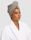 A person wears a white bathrobe and a Cozy Earth Waffle Hair Towel in light gray, wrapped around their head, looking slightly to the side with a neutral expression against a plain light gray background. |Color:Charcoal