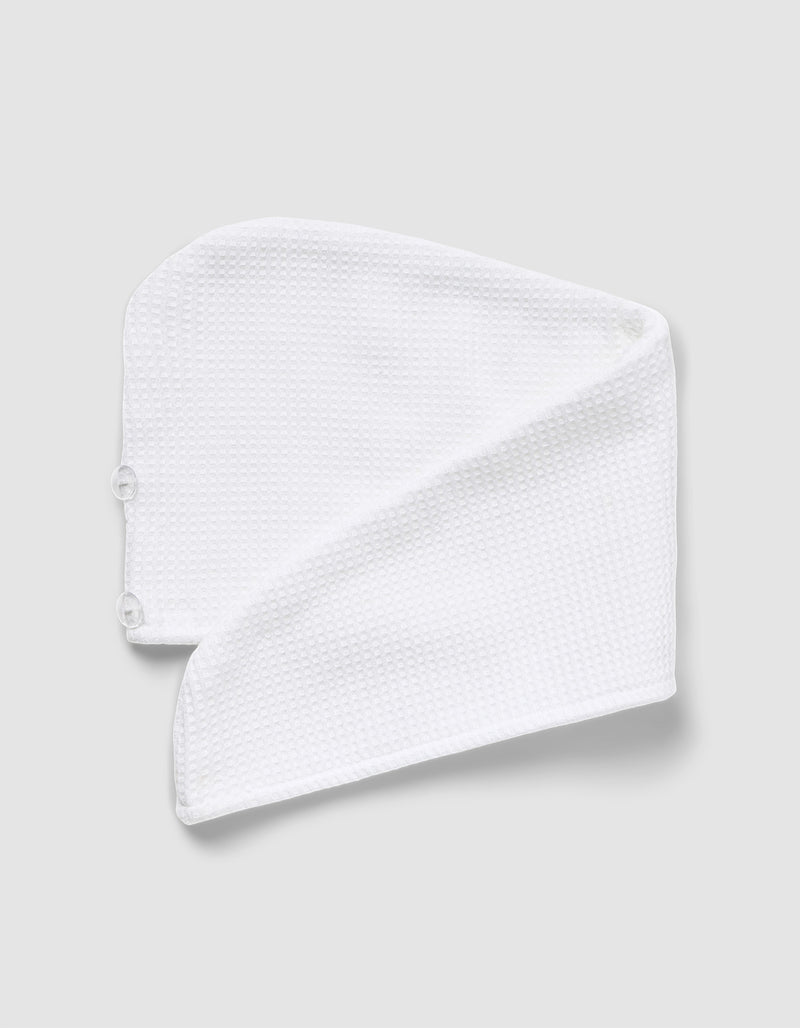 The Cozy Earth Waffle Hair Towel, made from white textured microfiber, is folded into a triangle with two buttons visible on one end and displayed against a light gray background.