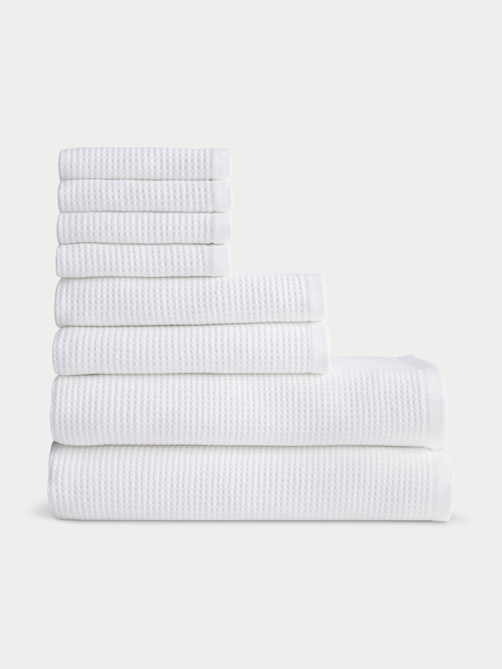 A neatly stacked set of Cozy Earth's Waffle Bath Towel Set, available in various sizes, is arranged in a stepped formation against a plain background. The towels feature a textured pattern and appear soft and fluffy.  