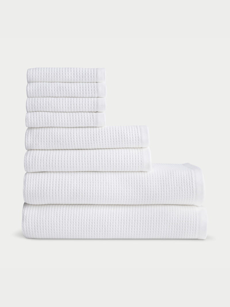 A neatly stacked set of Cozy Earth's Waffle Bath Towel Set, available in various sizes, is arranged in a stepped formation against a plain background. The towels feature a textured pattern and appear soft and fluffy.