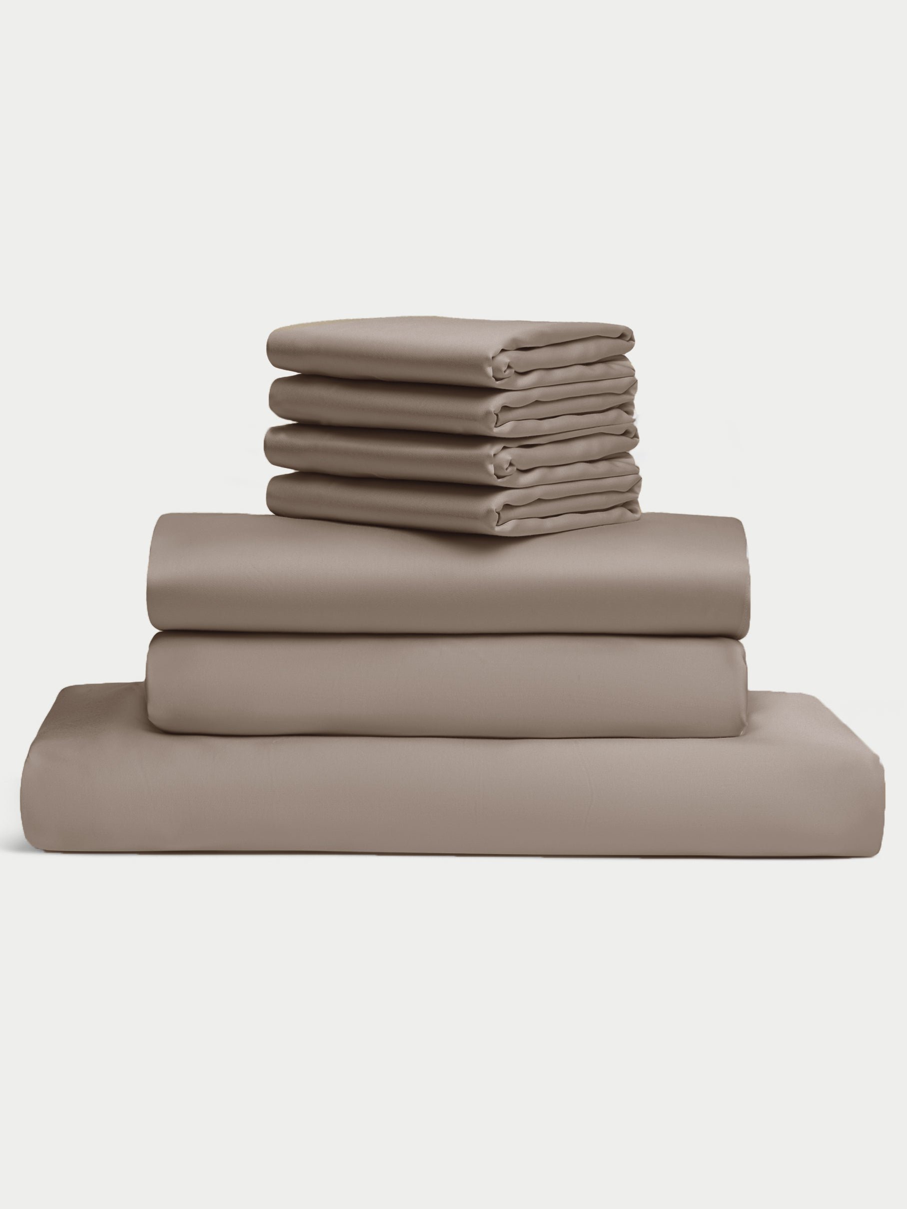 The Bamboo Bedding Core Bundle from Cozy Earth is displayed against a plain white background, featuring a neatly stacked set of folded taupe bed sheets, including pillowcases, a fitted sheet, and a flat sheet. |Color:Walnut