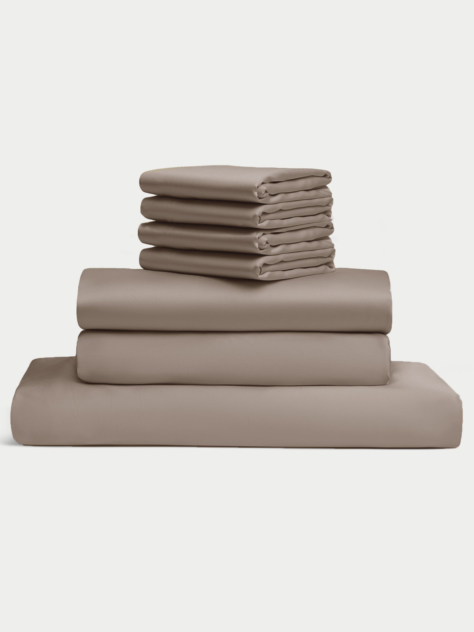 The Bamboo Bedding Core Bundle from Cozy Earth is displayed against a plain white background, featuring a neatly stacked set of folded taupe bed sheets, including pillowcases, a fitted sheet, and a flat sheet. 