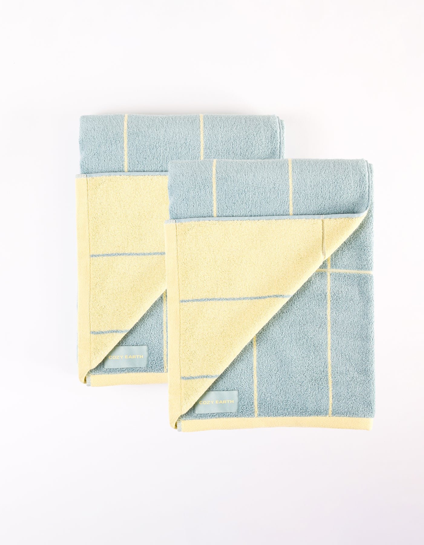 The Cozy Earth Windowpane Resort Towel Bundle features two neatly folded towels with a grid pattern in light blue and pale yellow, placed side by side on a white background. |Color:Blue Lagoon