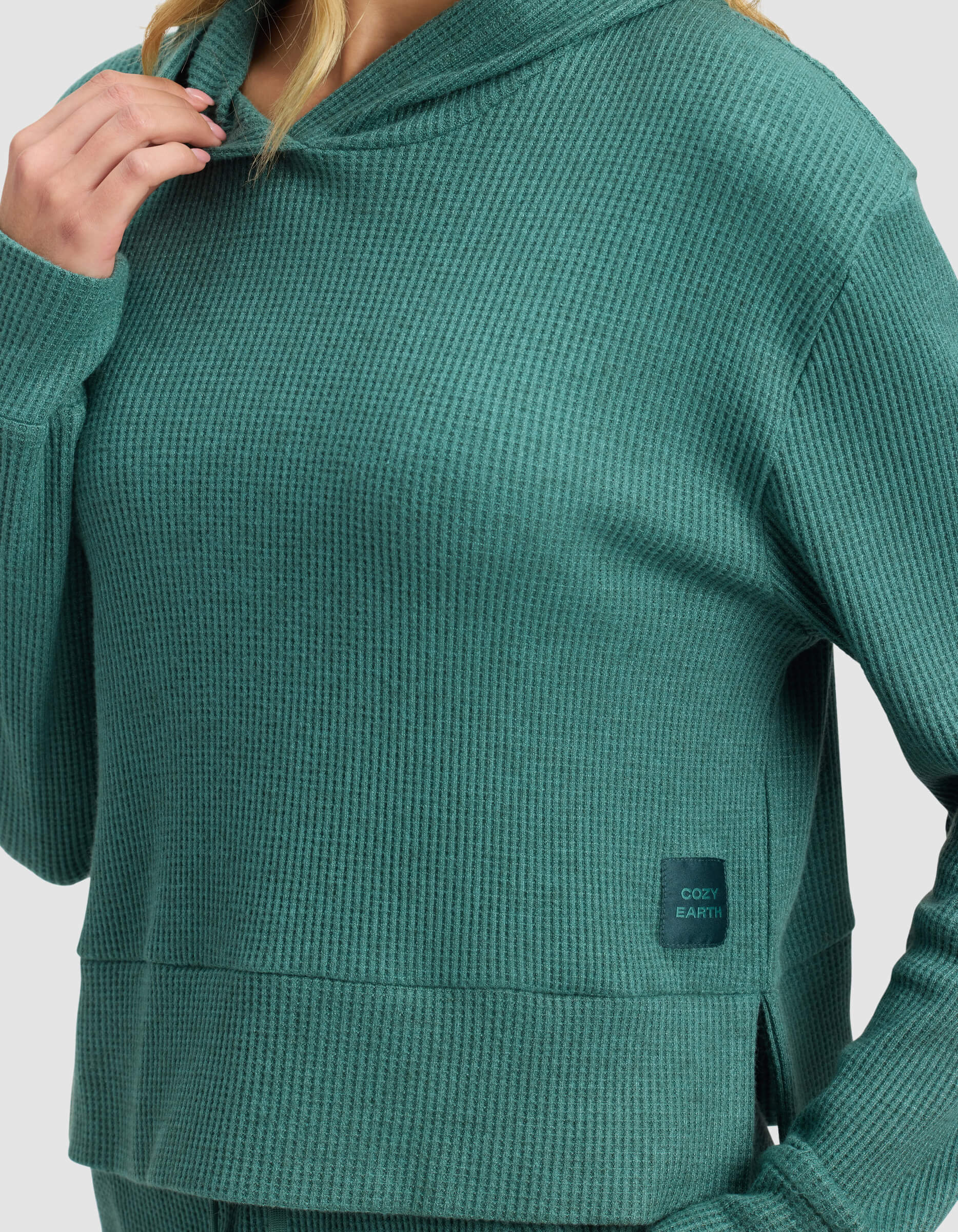 A person wears the Cozy Earth Women's Blake Waffle Hoodie in textured teal-green, featuring a "COZY EARTH" patch on the lower front. The face is partially out of view.|Color:Sea Green