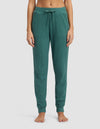 A person stands barefoot in Cozy Earth's Women's Blake Waffle Jogger, featuring a ribbed texture, green color, drawstring waist, and side pockets; shown from waist to feet against a plain light background.|Color:Sea Green