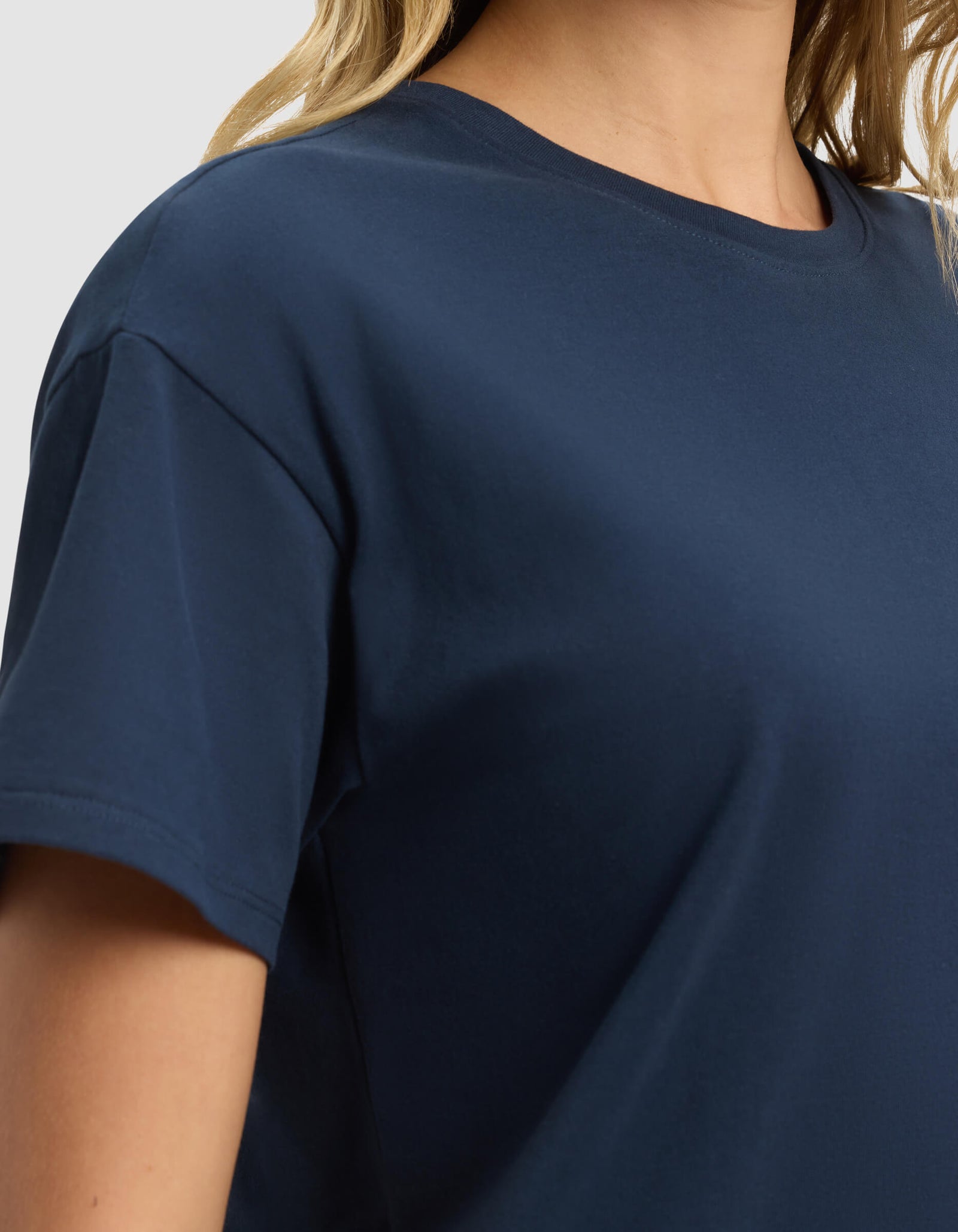 A close-up of a person wearing the Cozy Earth Women's All Day Tee in navy blue, highlighting the soft fabric and short sleeves. The image focuses on the upper torso, with the face not shown.