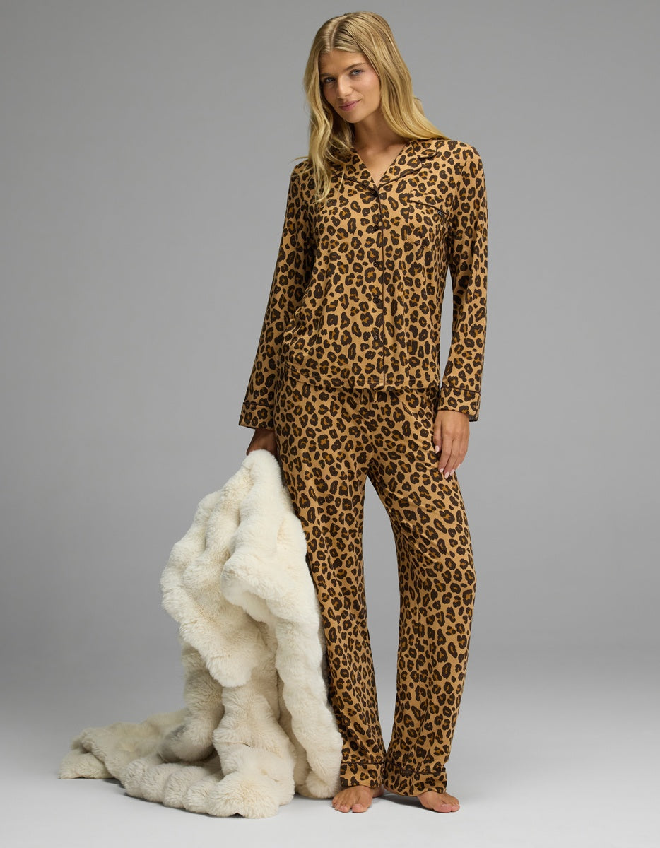 A person wearing a leopard-print button-down pajama top and matching Women’s Bamboo Stretch-Knit Pajama Pant, holding a fluffy white throw blanket.