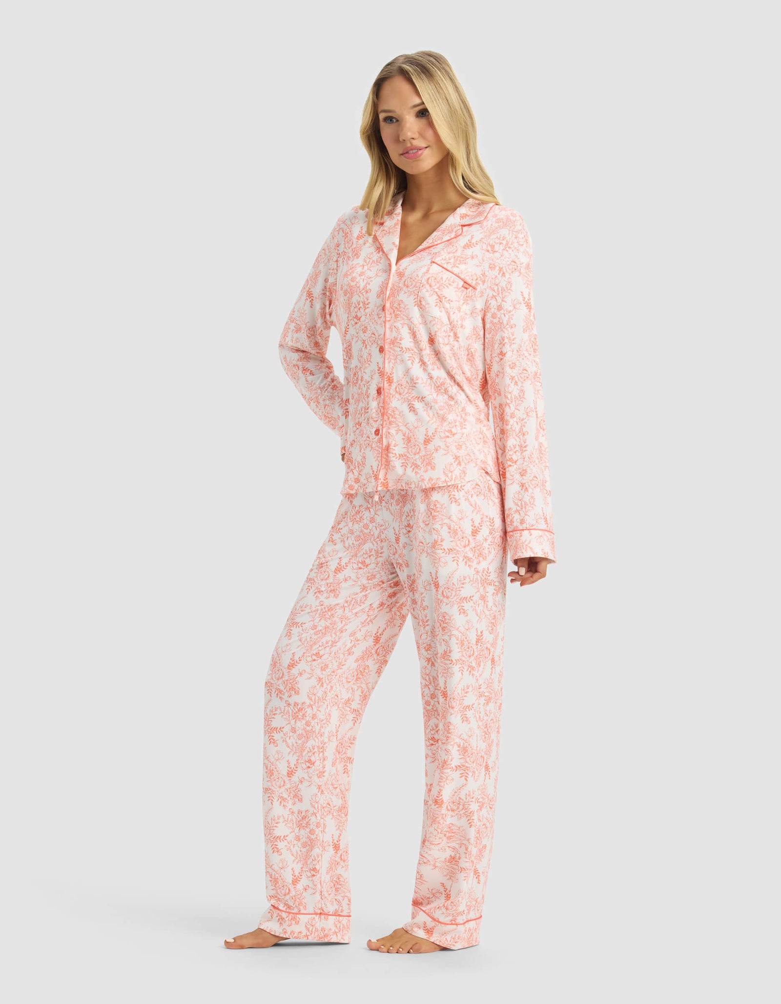 A woman poses barefoot against a gray background wearing the Cozy Earth Women's Bamboo Stretch-Knit Long Sleeve Pajama Set in light pink and white.