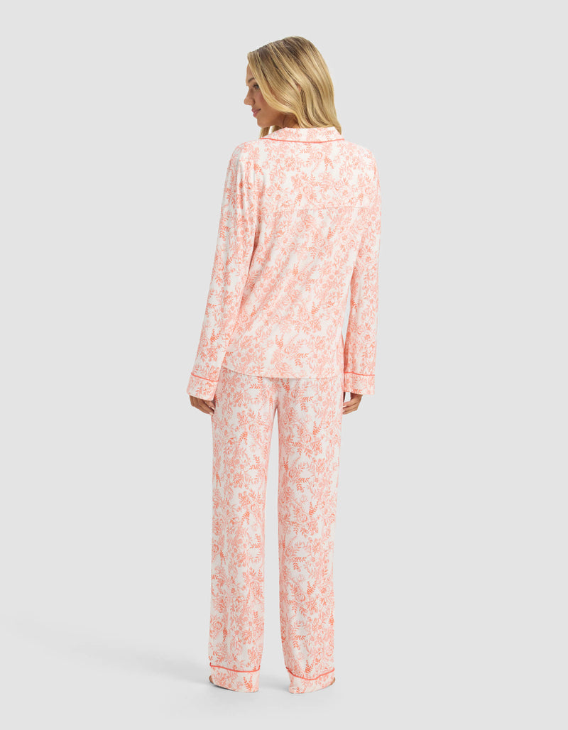 A woman faces away, wearing the Cozy Earth Women's Bamboo Stretch-Knit Long Sleeve Pajama Set featuring a light pink floral print on white, set against a plain light grey background.