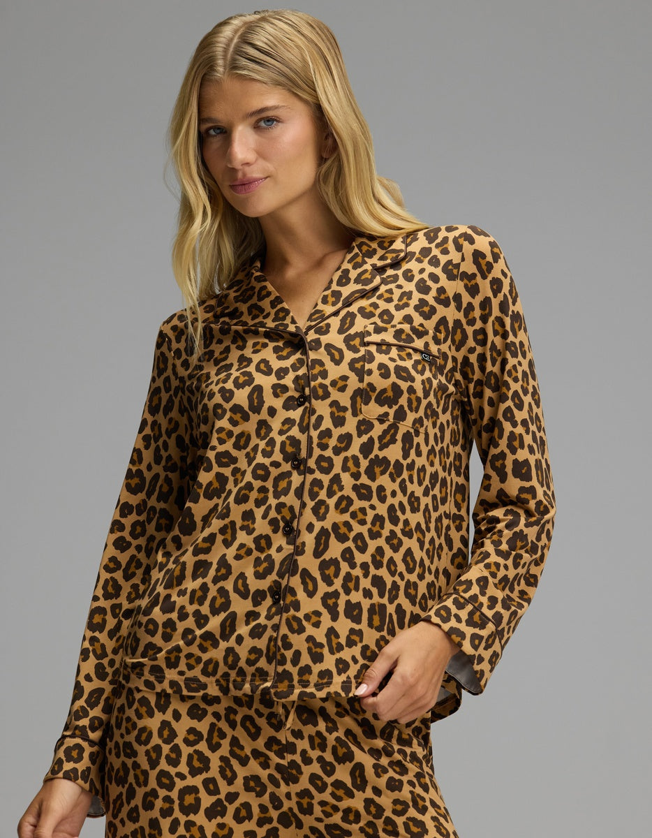 A woman wearing a Cozy Earth Women’s Bamboo Stretch-Knit Long Sleeve Pajama Top in a tan and brown leopard print, featuring a long-sleeved button-up design with a collared neckline and a chest pocket.
