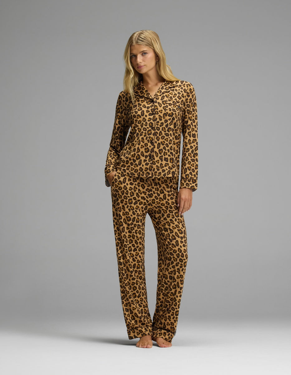 A woman wearing a brown and black leopard print Women’s Bamboo Stretch-Knit Long Sleeve Pajama Set consisting of a long-sleeved button-up top and matching pants.|Color:Leopard Print in Chocolate