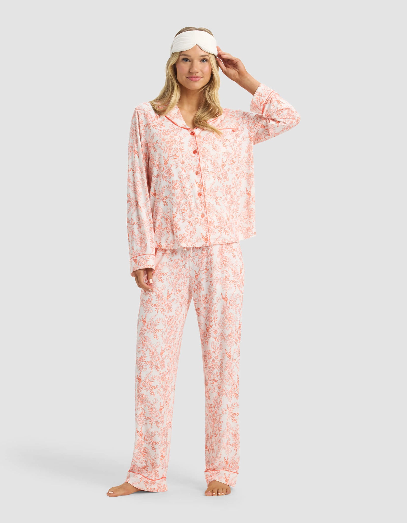 A woman smiles barefoot in Cozy Earth Women's Bamboo Stretch-Knit Pajama Pant with a white sleep mask pushed up on her forehead, standing against a plain light background.
