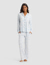 A woman stands barefoot, hands in her pockets, wearing the Cozy Earth Women's Bamboo Stretch-Knit Long Sleeve Pajama Set in a light blue and white pattern, against a plain light gray background.|Color:Sky Toile