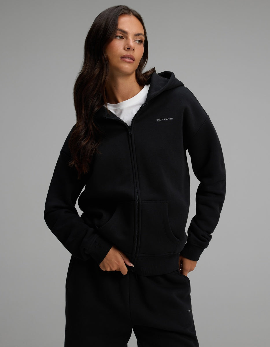 A woman wearing a black Cozy Earth Women’s CityScape Full-Zip Hoodie over a white t-shirt.