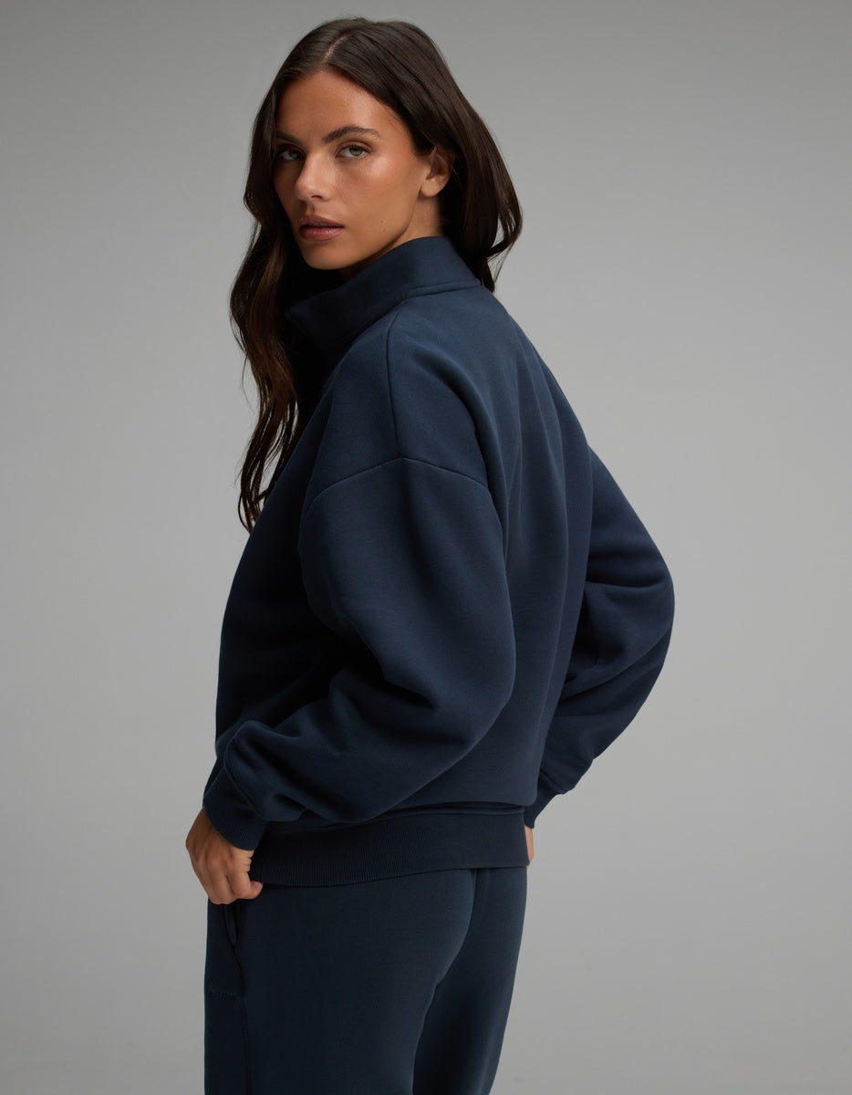 A woman viewed from the side, wearing a dark blue Cozy Earth Women’s CityScape Quarter Zip with a high collar.
