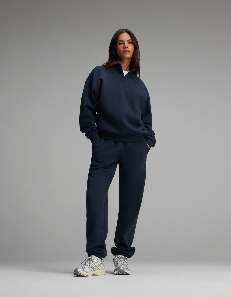 A person wearing a dark blue Cozy Earth Women’s CityScape Quarter Zip long-sleeve pullover and matching drawstring sweatpants with grey athletic sneakers.