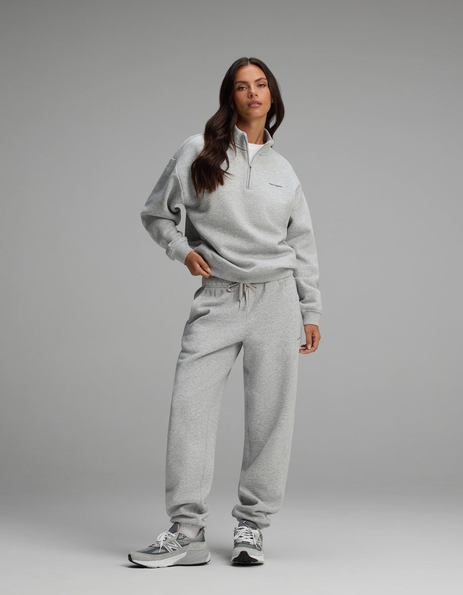 A woman wearing a light gray Cozy Earth Women’s CityScape Quarter Zip and matching sweatpants with gray and white sneakers.