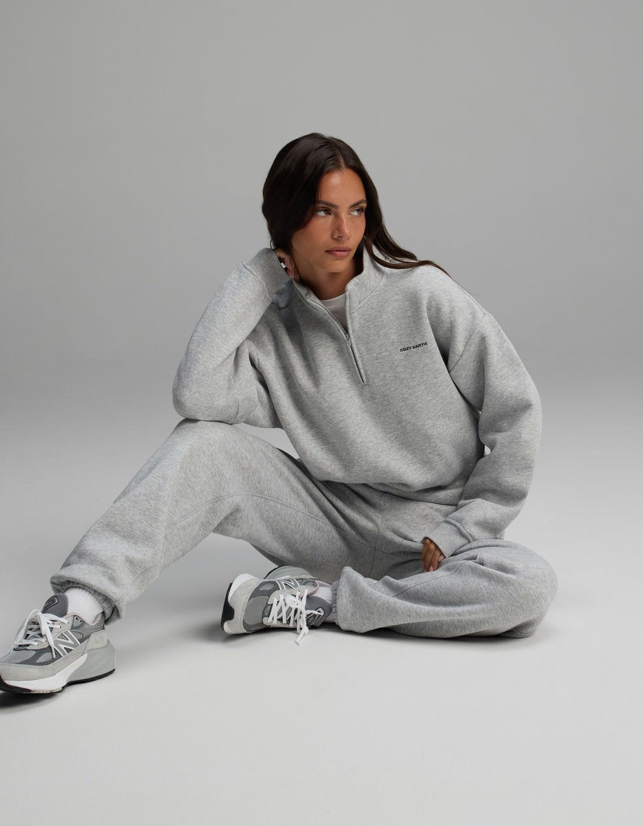 A person wearing a grey Women’s CityScape Quarter Zip and matching joggers sits on the floor.