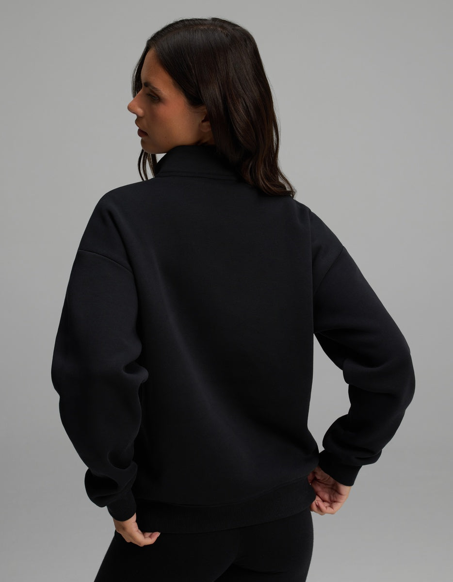 A person from behind wearing a black Cozy Earth Women’s CityScape Quarter Zip, featuring a long-sleeved pullover design with ribbed cuffs and hem.