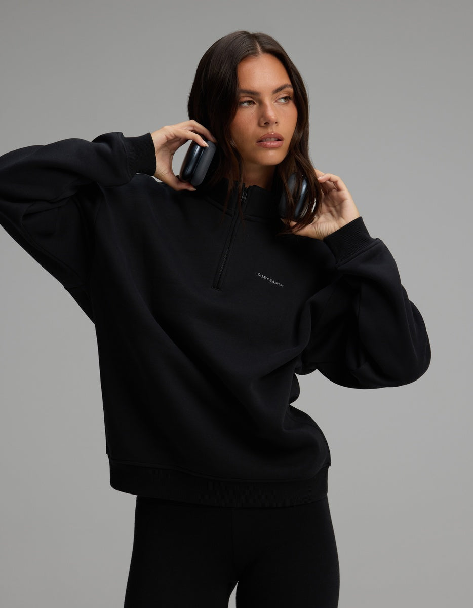 A woman wearing a black Women’s CityScape Quarter Zip with headphones around her neck.