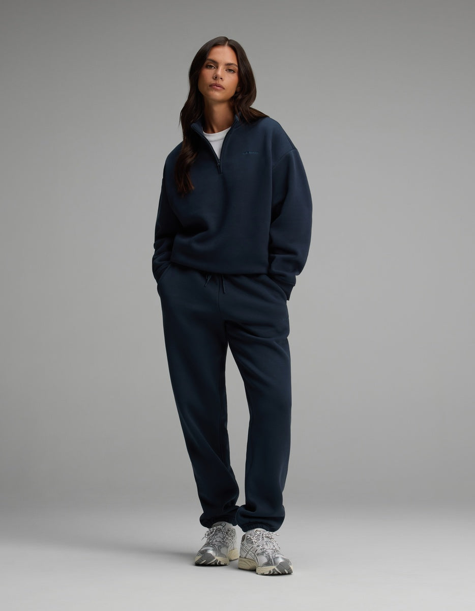 A model wears a dark blue Cozy Earth Women’s Cityscape Quarter Zip & Sweatpant Set with silver athletic shoes.