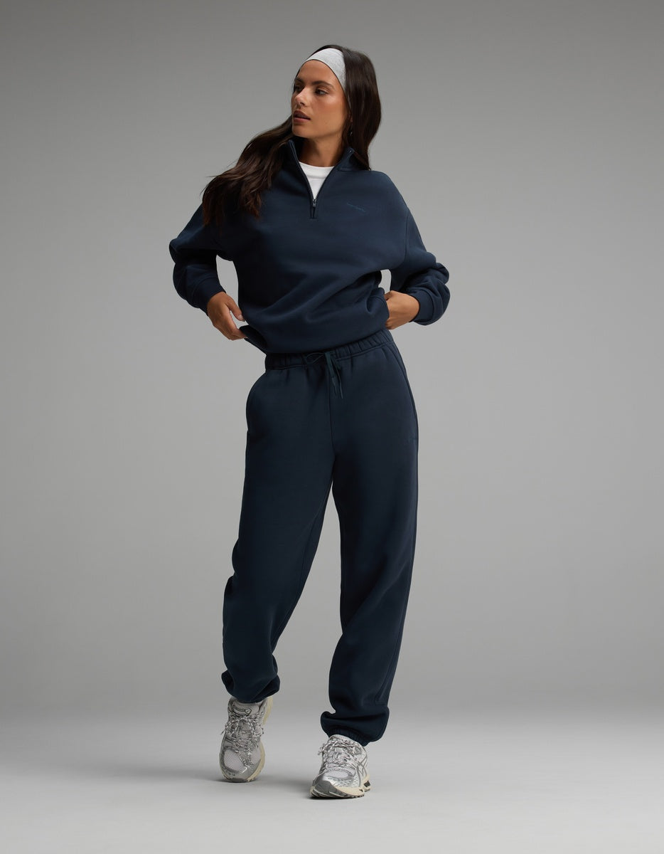 A person wearing a dark navy Cozy Earth Women’s Cityscape Quarter Zip & Sweatpant Set and gray athletic sneakers.