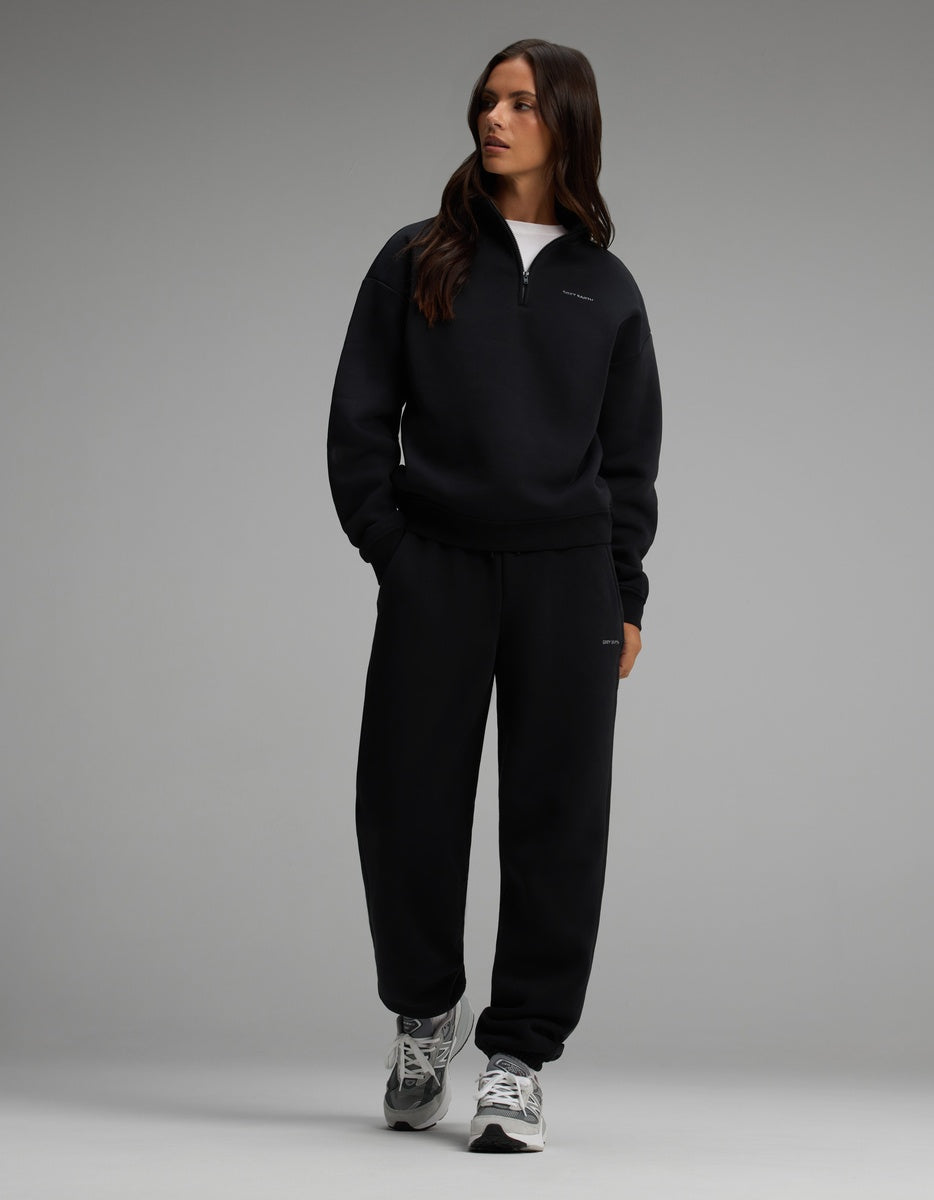A woman wearing a black Cozy Earth Women’s Cityscape Quarter Zip & Sweatpant Set with grey athletic shoes.