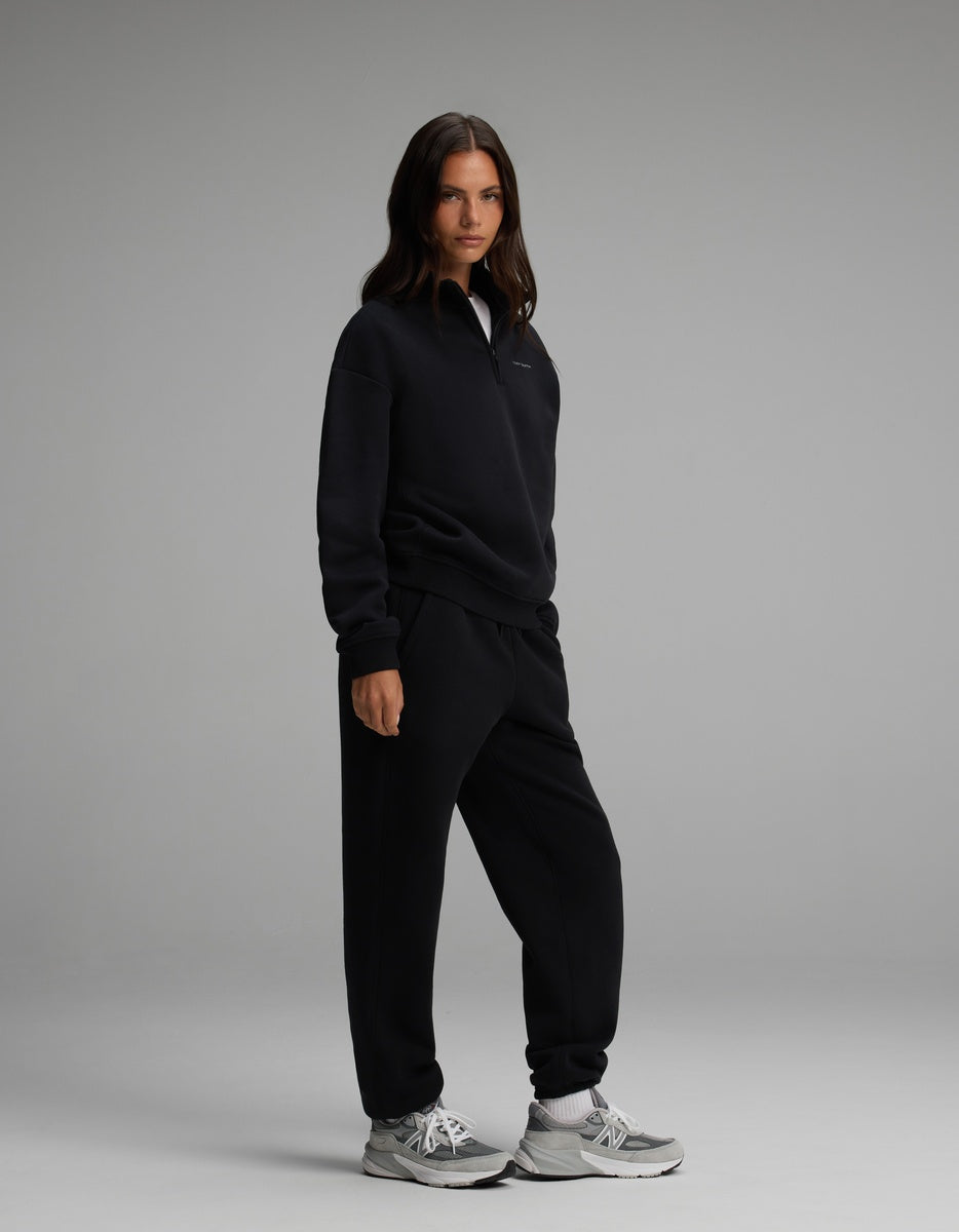 A woman wearing a black Cozy Earth Women’s Cityscape Quarter Zip & Sweatpant Set and grey athletic sneakers.