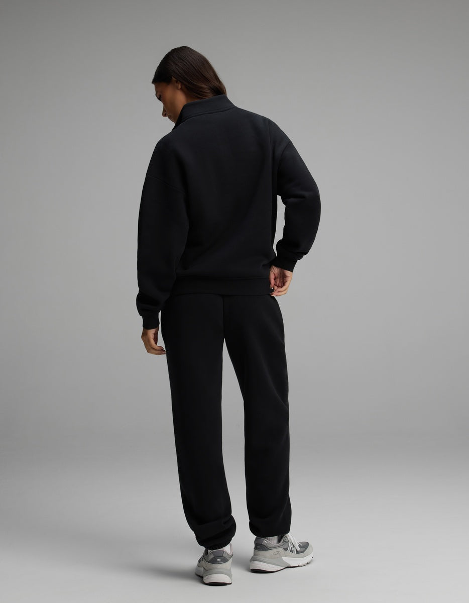 A person wearing a black Cozy Earth Women’s Cityscape Quarter Zip & Sweatpant Set with grey sneakers.
