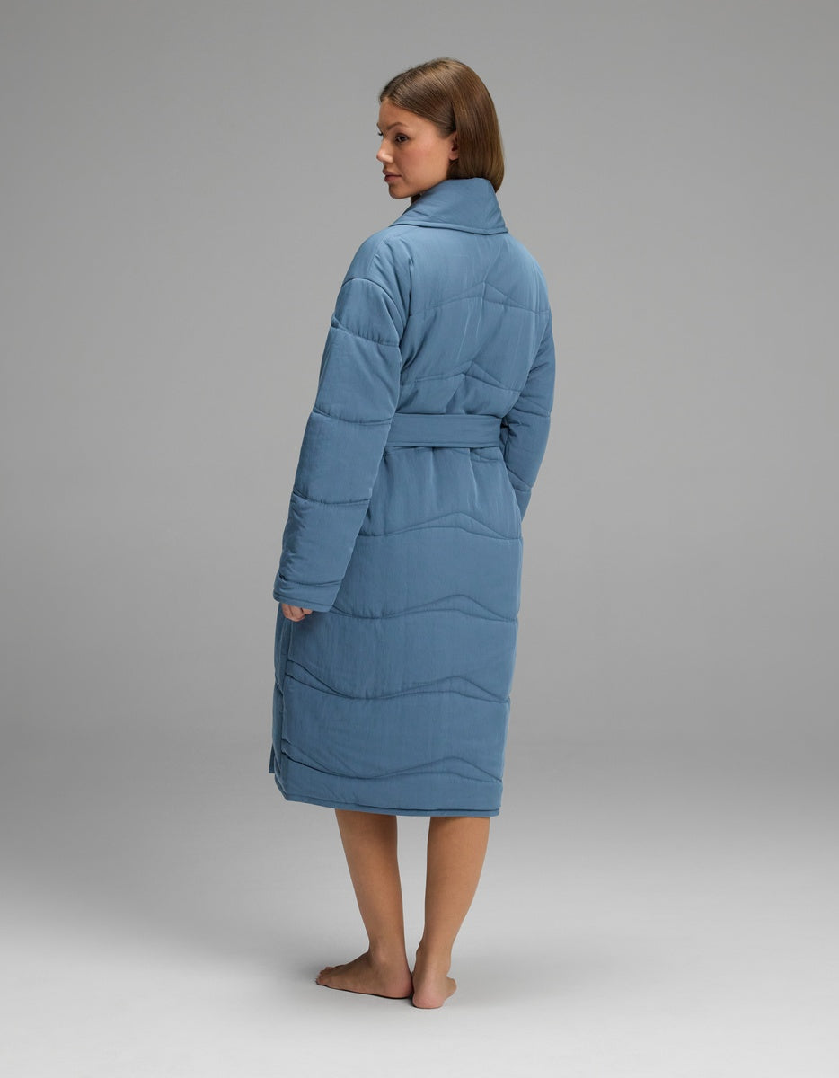 A person seen from the back wearing a blue, knee-length Cozy Earth Women’s Quilted House Coat with a tie waist and a wide collar.