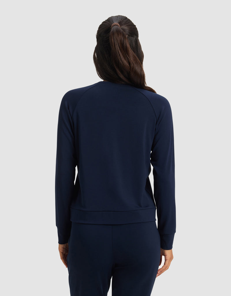 A woman with long brown hair in a ponytail is shown from the back, wearing Cozy Earth's Women's Brushed Bamboo Pullover Crew in navy blue against a plain light gray background.
