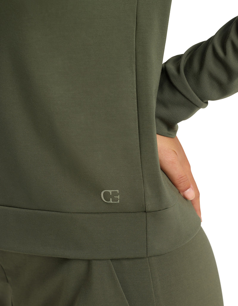 Close-up of a person in the Cozy Earth Women's Brushed Bamboo Pullover Crew in olive green, hand on hip. A small "CE" logo appears near the hem of the top against a white background.