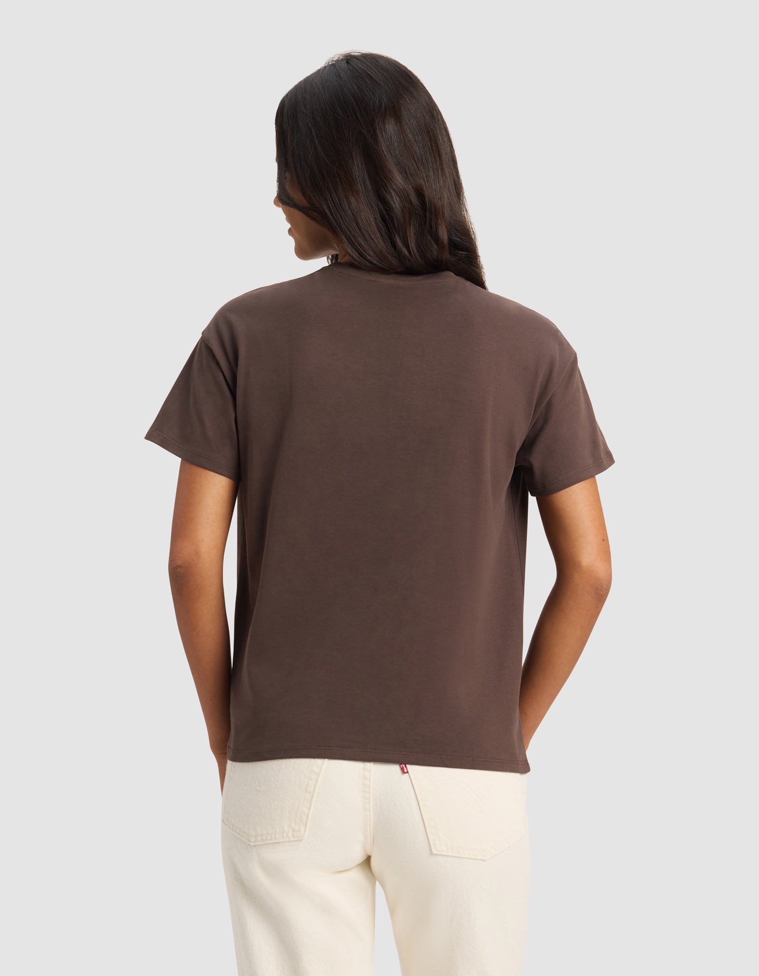 A woman with long dark hair, wearing the Cozy Earth Women's All Day Tee in brown and light-colored jeans, stands facing away from the camera against a plain light background.|Color:Cacao