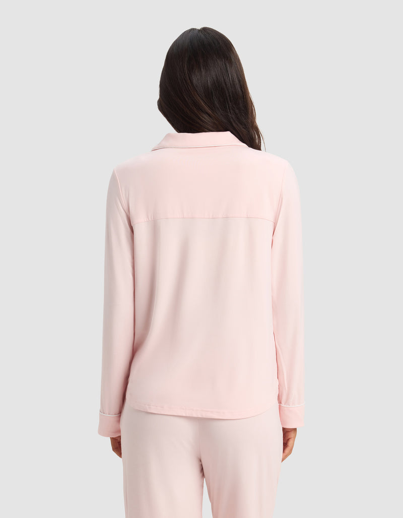 A woman with long dark hair stands with her back to the camera, wearing the Cozy Earth Women's Bamboo Stretch-Knit Long Sleeve Pajama Set in light pink against a plain light gray background.