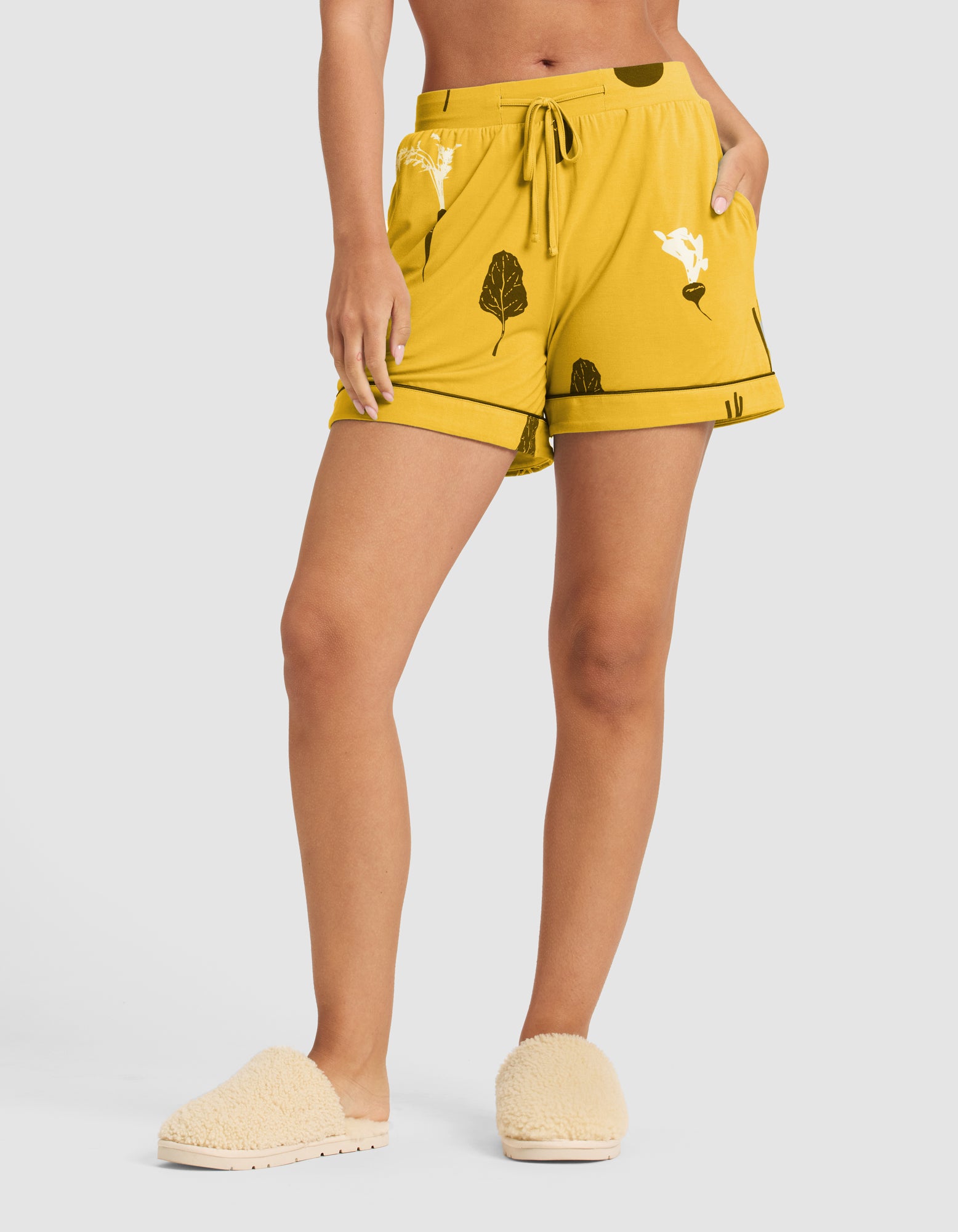 A person wears HIDE’s Last Chance Women's Bamboo Stretch-Knit Pajama Short (Veggie), featuring a drawstring waist and pockets, paired with beige fuzzy slippers. The upper body is partially out of frame. |Color:Veggies in Mango