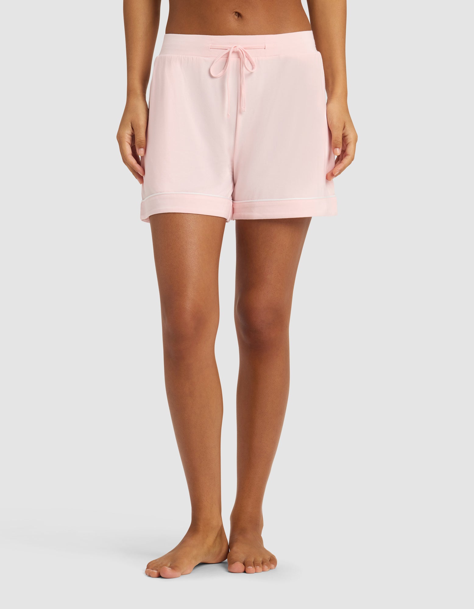 A person wearing Cozy Earth Women's Bamboo Stretch-Knit Pajama Shorts in pale pink stands barefoot on a light grey background; the image is cropped from the waist down.