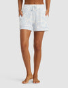 A person is shown from waist to feet, barefoot, wearing Cozy Earth Women's Bamboo Stretch-Knit Pajama Shorts in light blue and white pattern with a drawstring waist and pockets, hands in pockets, against a plain background.|Color:Sky Toile
