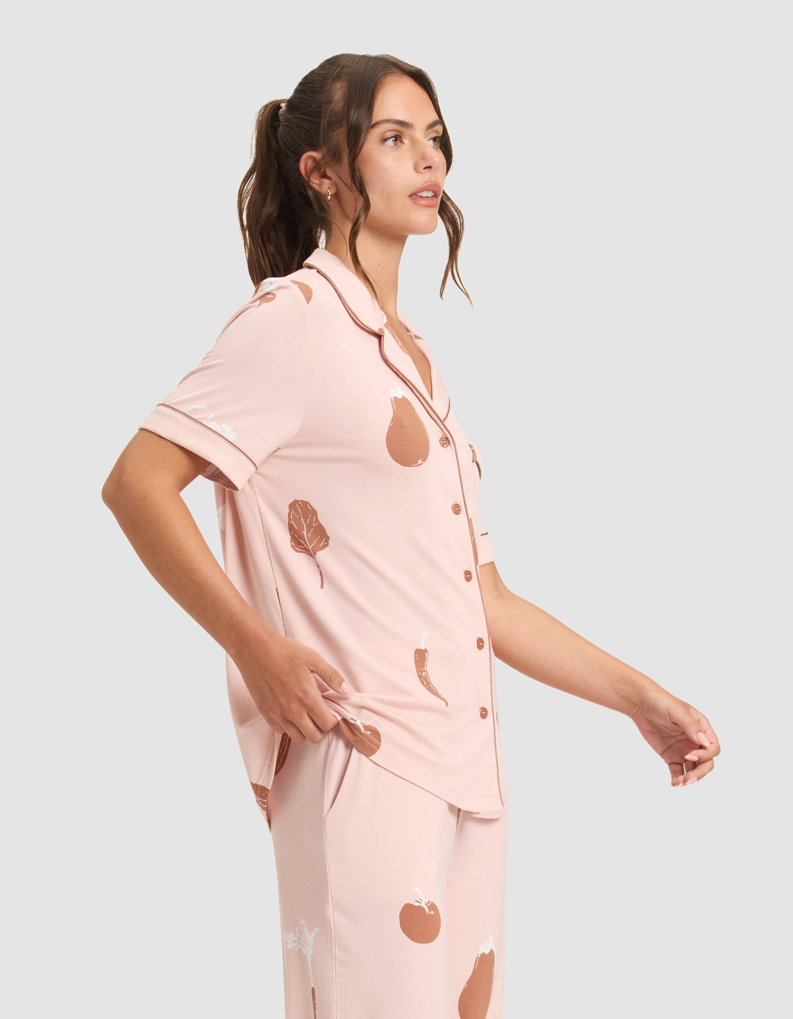 A woman models the HIDE Women's Bamboo Stretch-Knit Short Sleeve Pajama Top, featuring a pink color with brown vegetable prints, against a light gray background, looking to the side with a relaxed pose. |Color:Veggies in Dusty Rose
