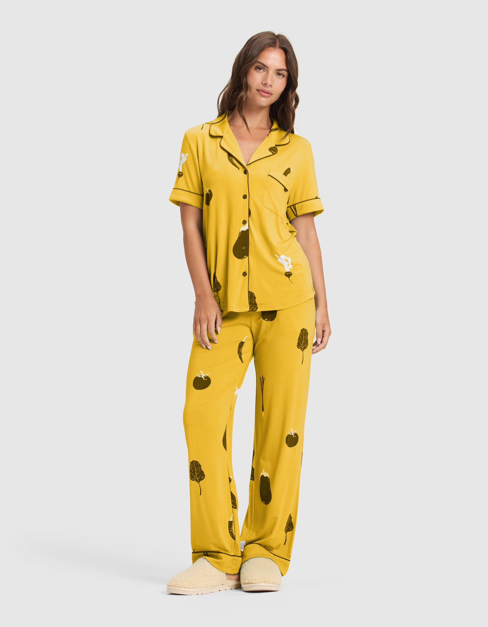 A woman wears the Women's Bamboo Stretch-Knit Short Sleeve Pajama Top (Veggie), featuring a loose fit and black and white abstract veggie designs, with matching slippers, against a plain light background.