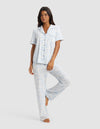 A woman poses barefoot against a plain light background, wearing the Cozy Earth Women's Bamboo Stretch-Knit Short Sleeve & Pant Pajama Set in a light blue and white pattern.|Color:Sky Toile
