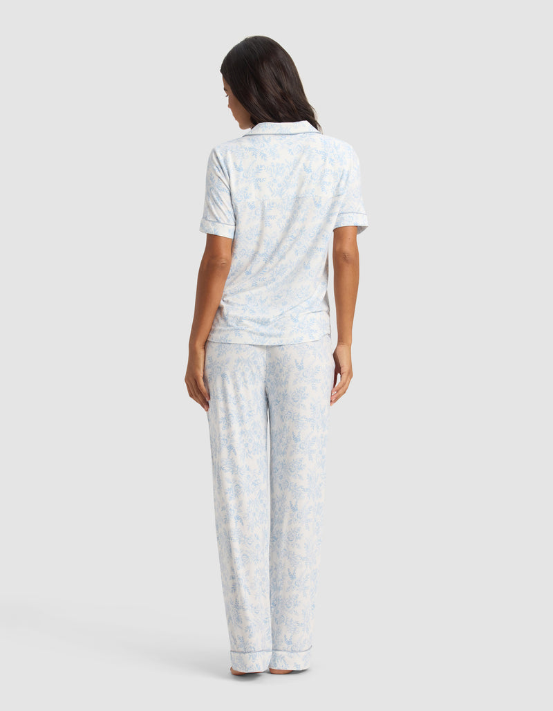 A woman faces away wearing the Cozy Earth Women's Bamboo Stretch-Knit Short Sleeve & Pant Pajama Set in light blue and white, shown against a plain light gray background.