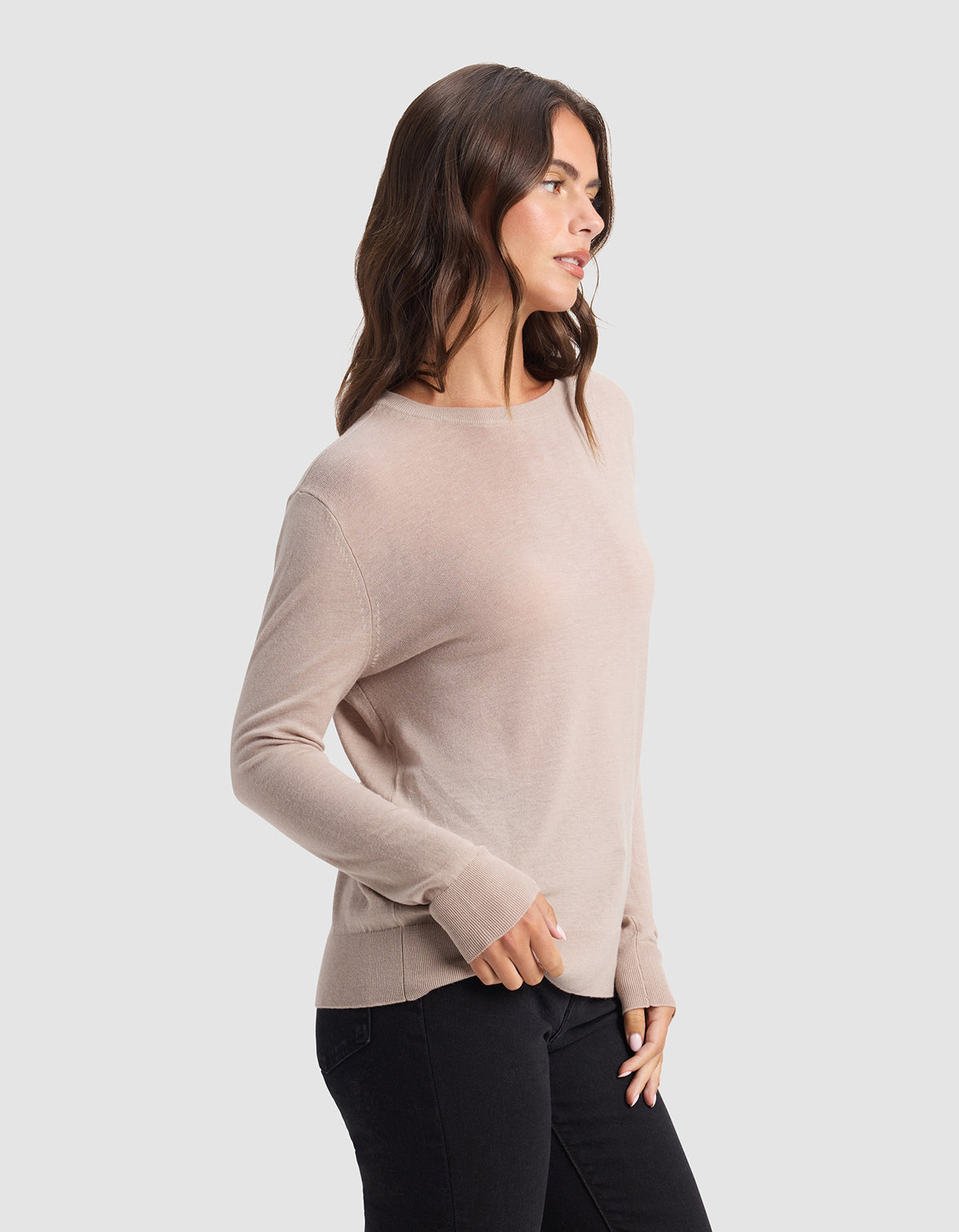 A woman with long brown hair wears the Cozy Earth Women's AirKnit Crewneck Sweater in light beige with black jeans, standing sideways against a plain light gray background.|Color:Taupe