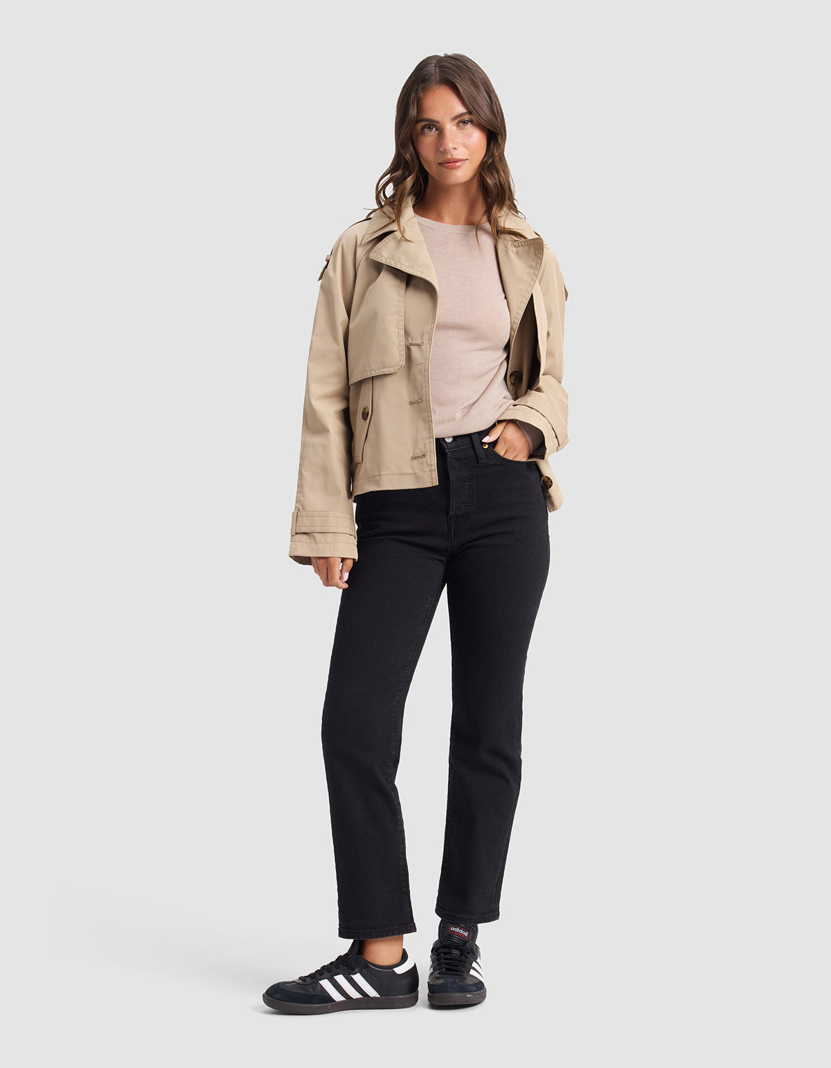 A woman faces forward, wearing the Cozy Earth Women's AirKnit Crewneck Sweater in beige, black jeans, and black Adidas sneakers with white stripes, standing against a plain gray background.|Color:Taupe