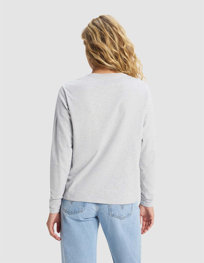 A person with wavy blonde hair is shown from the back, wearing the Cozy Earth Women's All Day Long Sleeve Tee in light gray and light blue jeans against a plain light background.
