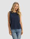 A woman with long blonde hair models the Cozy Earth Women's All Day Sleeveless Tee in navy blue and blue jeans, standing against a plain light gray background and looking forward with a slight smile.|Color:Eclipse