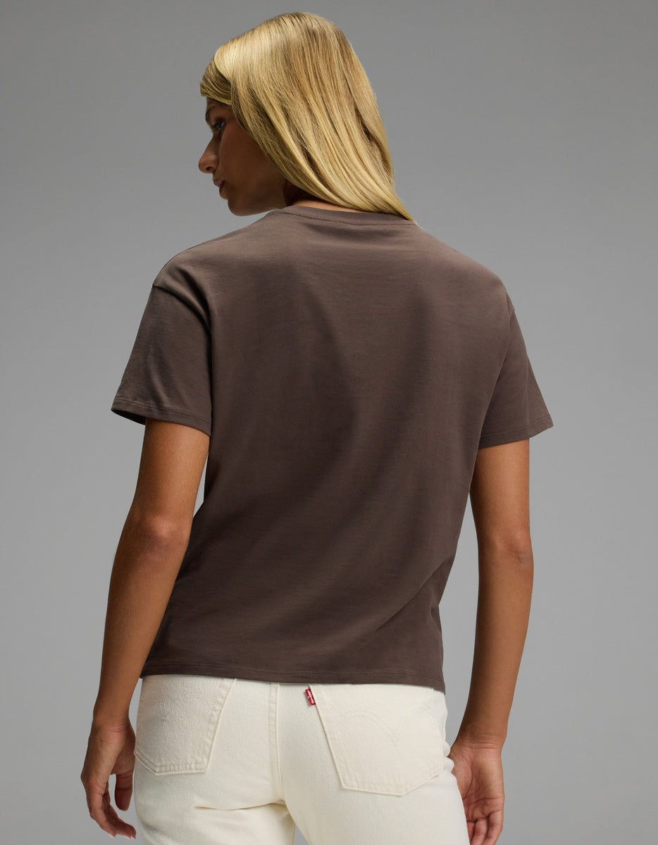 A person with straight blonde hair wears the Cozy Earth Women’s All Day Tee in brown and off-white jeans, standing with their back to the camera against a plain gray background.
