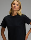 A woman with long blonde hair wears the Women’s All Day Tee by Cozy Earth in black and gazes slightly to the side against a plain gray background.|Color:Jet Black